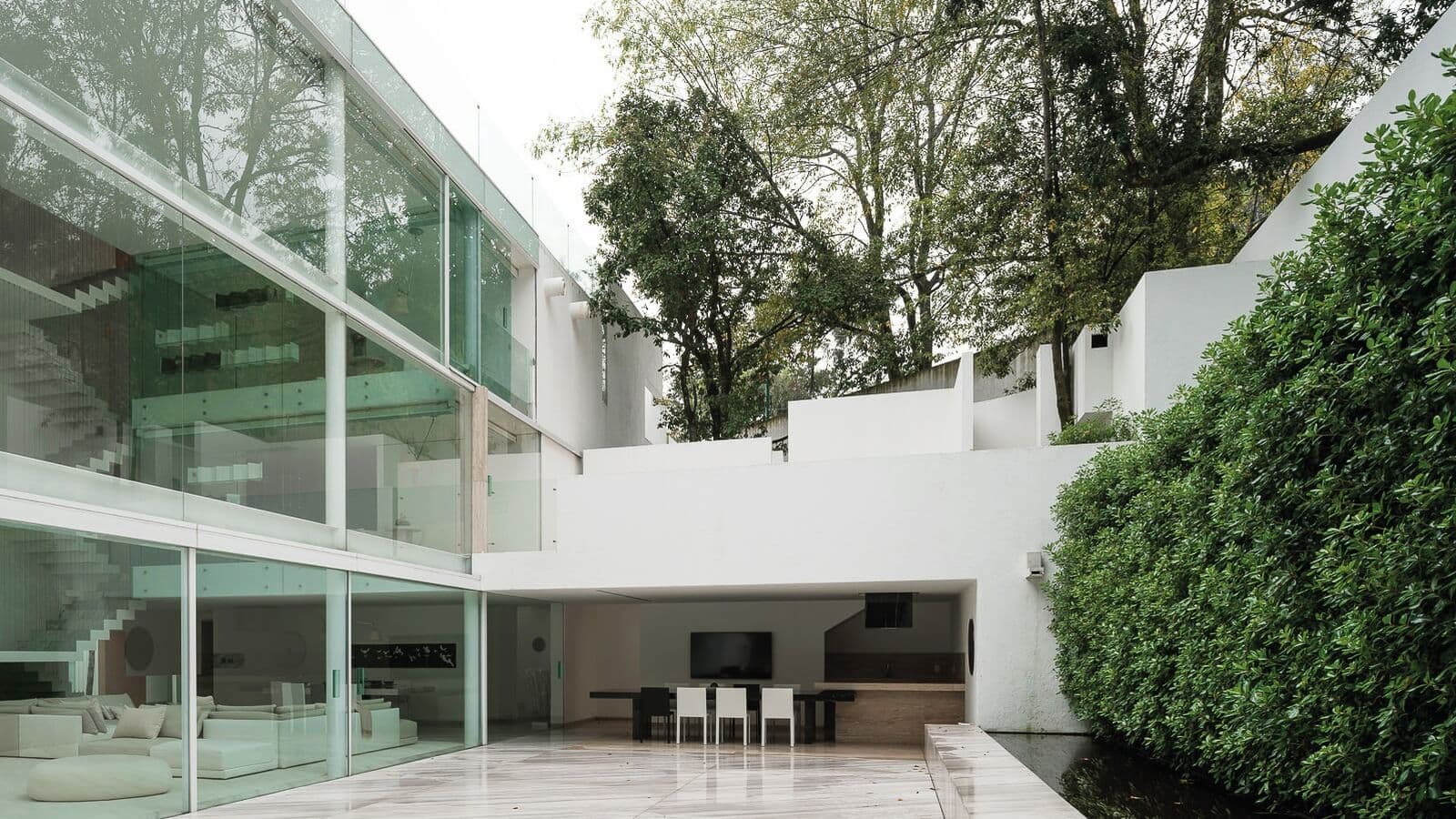 Residencia privada en Ciudad de México con fachada de cristal, patio exterior, vegetación y arquitectura contemporánea.