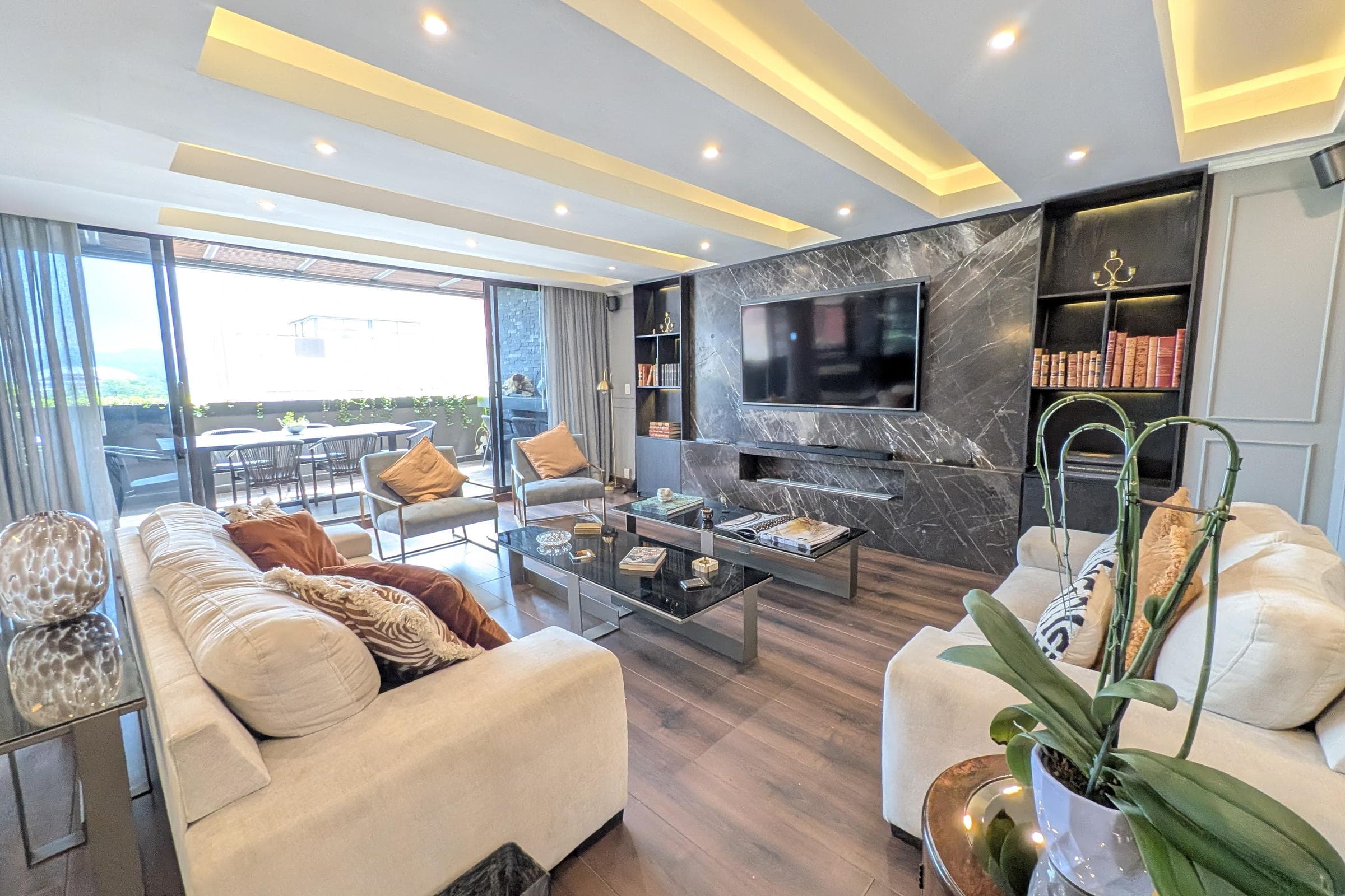 Sala con muro de mármol oscuro, sofás en tono crema y salida a la terraza.