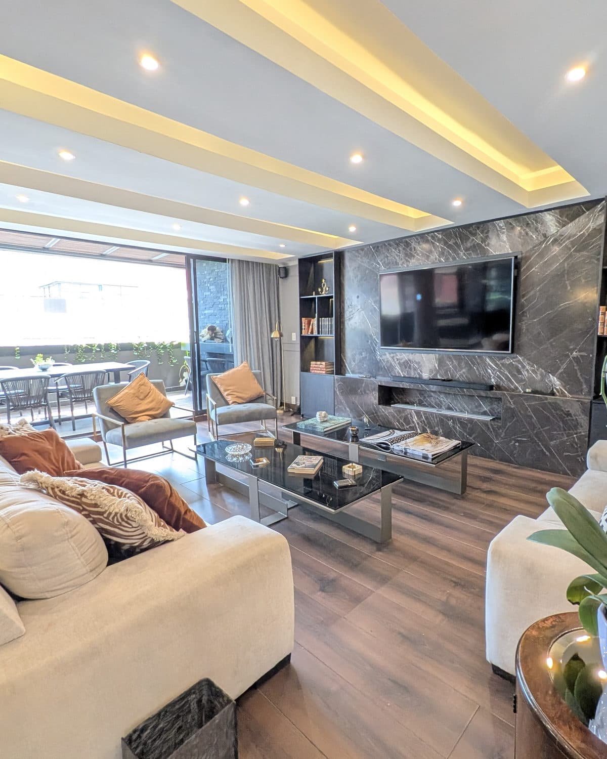 Sala con muro de mármol oscuro, sofás en tono crema y salida a la terraza.
